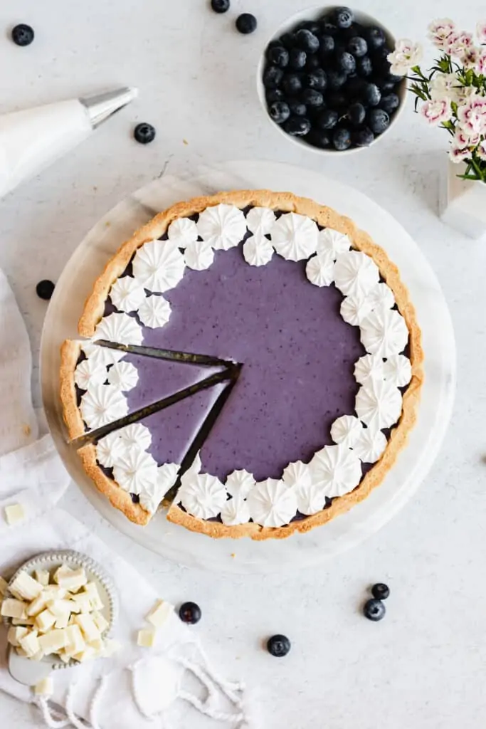 Blueberry white chocolate ganache tart from above. Two slices are cut. White chocolate and blueberries are in the background.