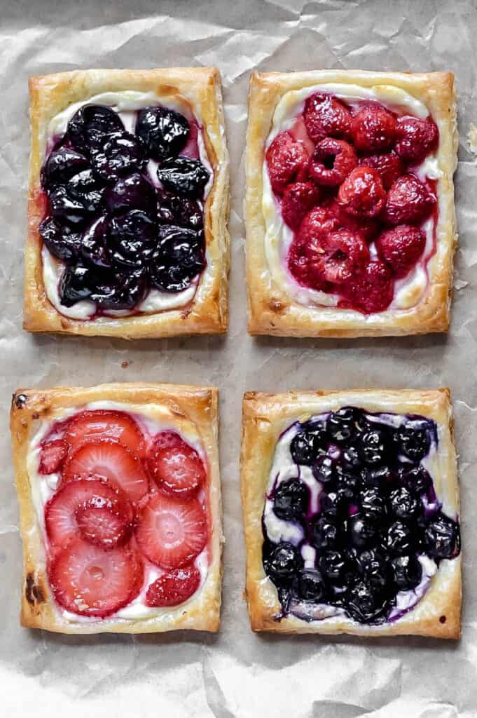Overhead shot of four baked fruit & cream cheese puff pastry danish. Strawberry, blueberry, raspberry, and cherry