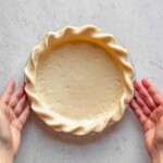 Hands hold a crimped pie crust.