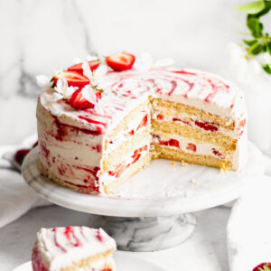 Strawberry Shortcake layer cake on a cake stand with a slice removed.