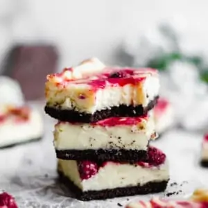 A stack of three raspberry white chocolate cheesecake bars. The top bar has a bite out of the top.