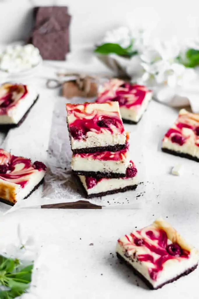 Stack of three raspberry white chocolate cheesecake bars with other pieces of bars scattered around