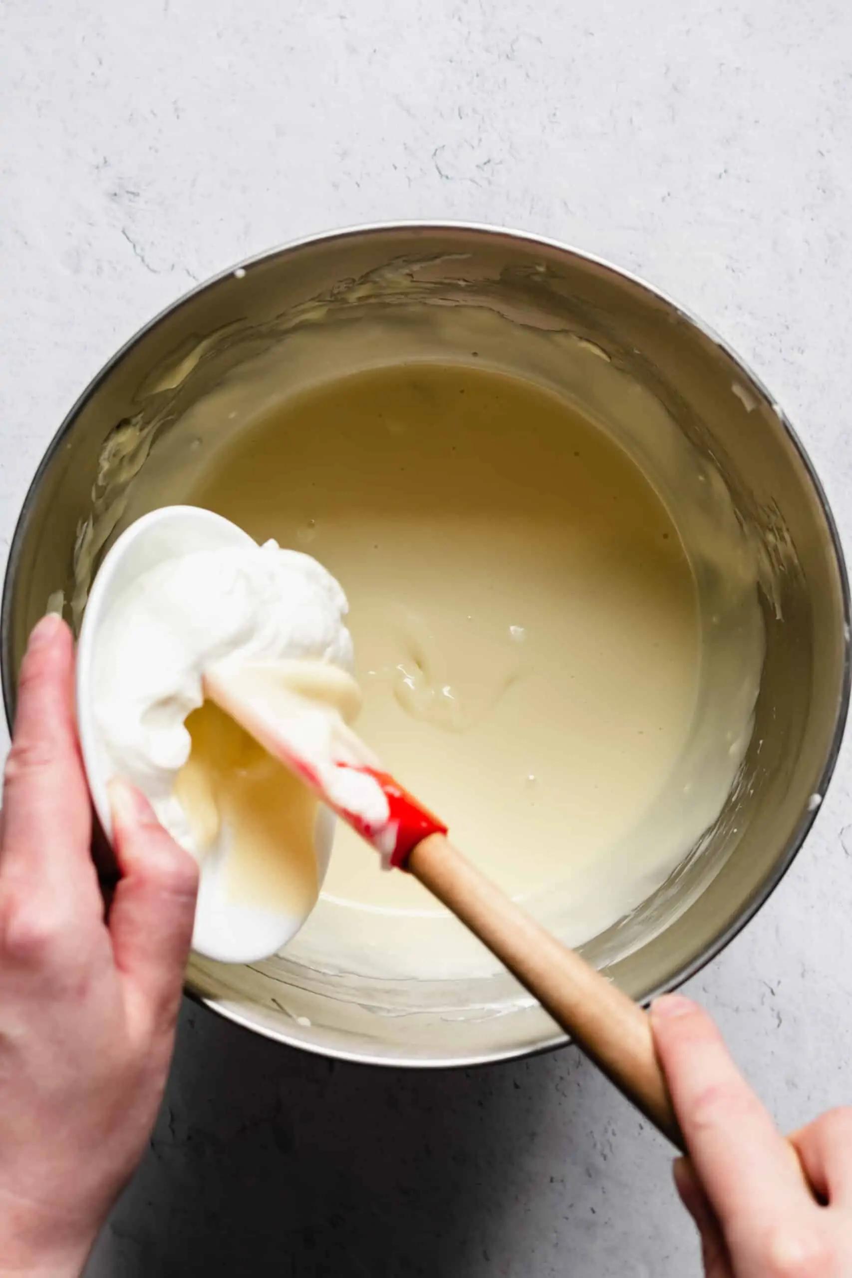 Sour cream being added to cheesecake batter in a bowl.