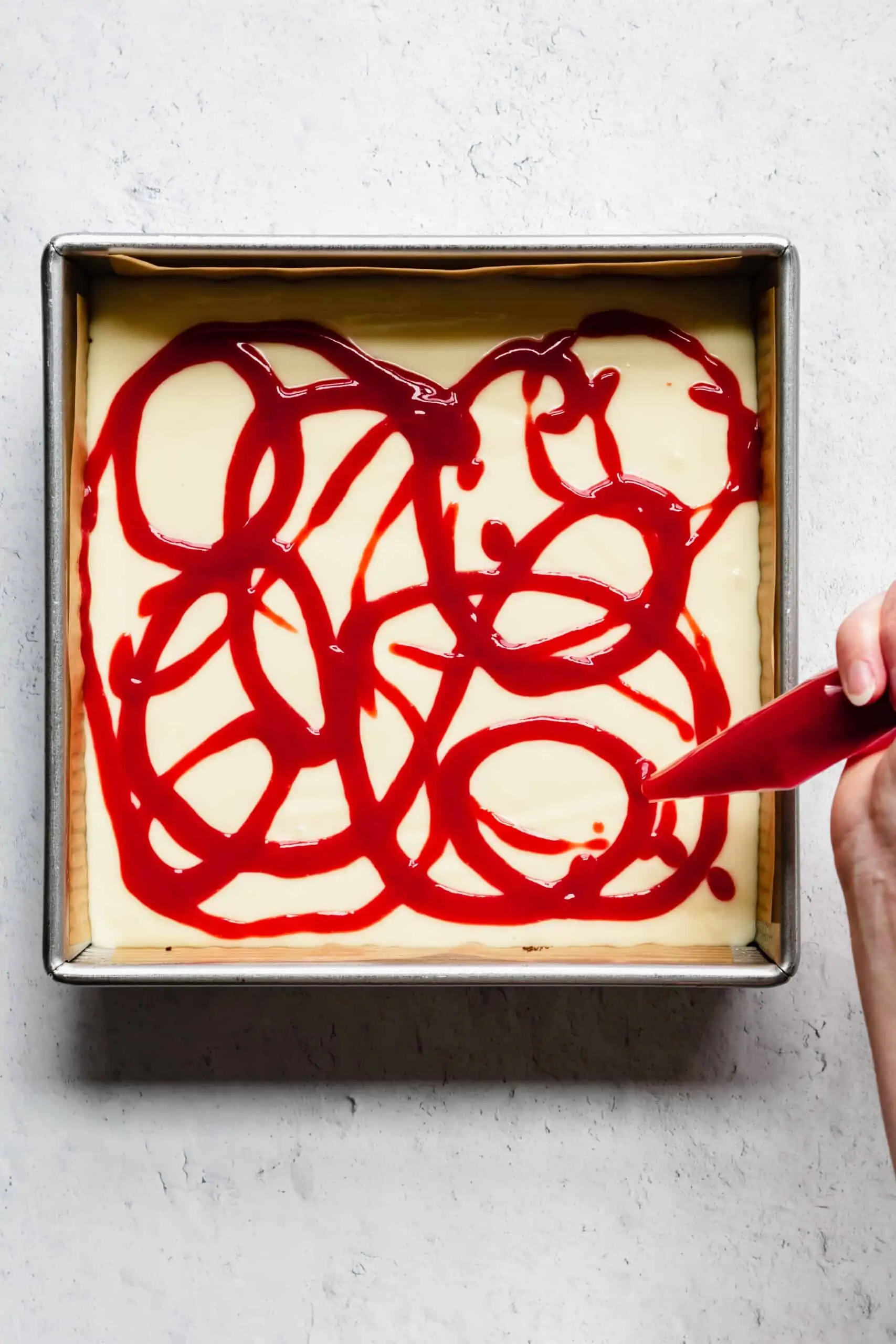 Raspberry puree being added to cheesecake in squiggles with a piping bag.