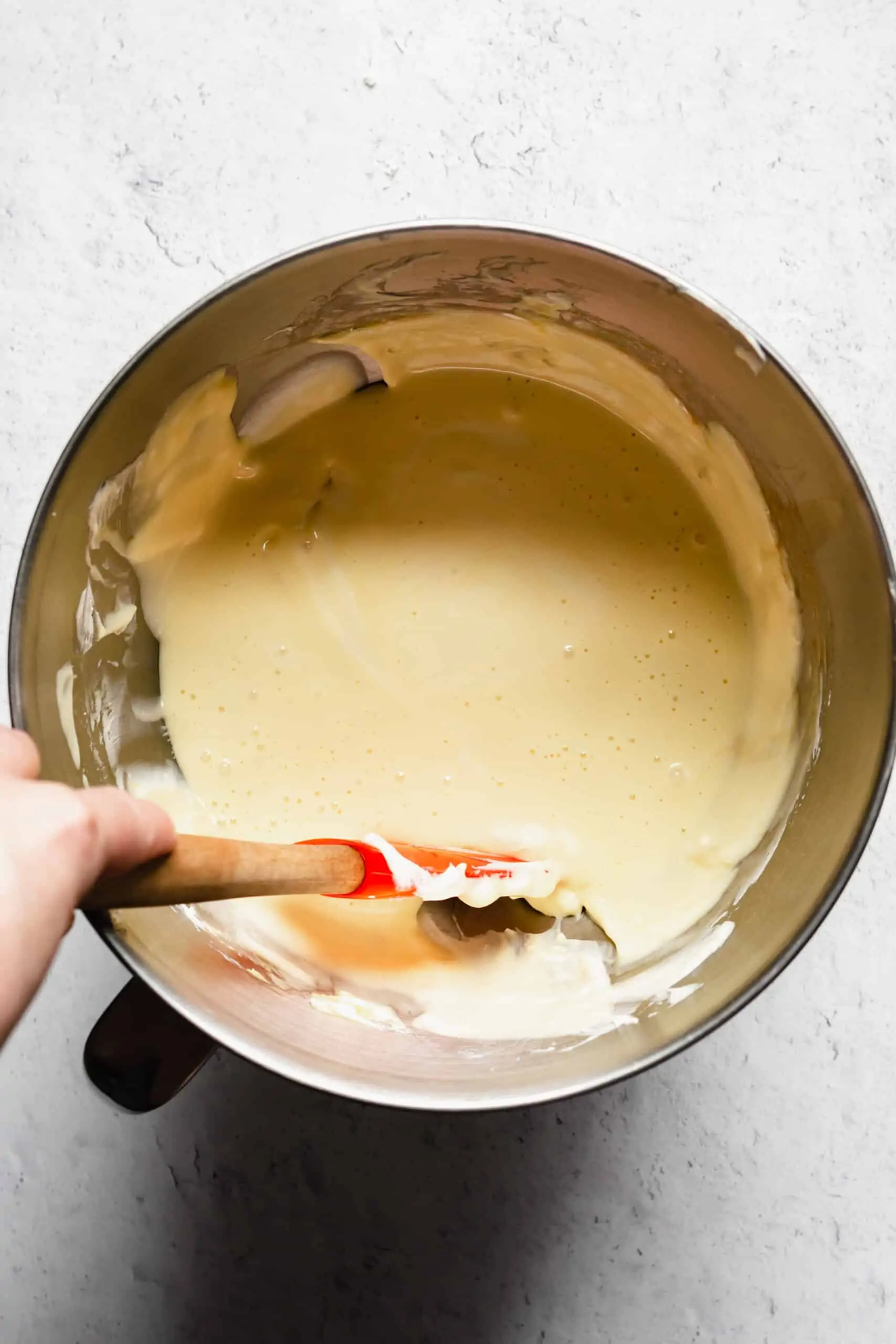 Cheesecake batter in a bowl with sides being scraped down.