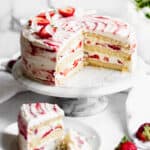 Strawberry shortcake layer cake on a stand with slices removed to show the center