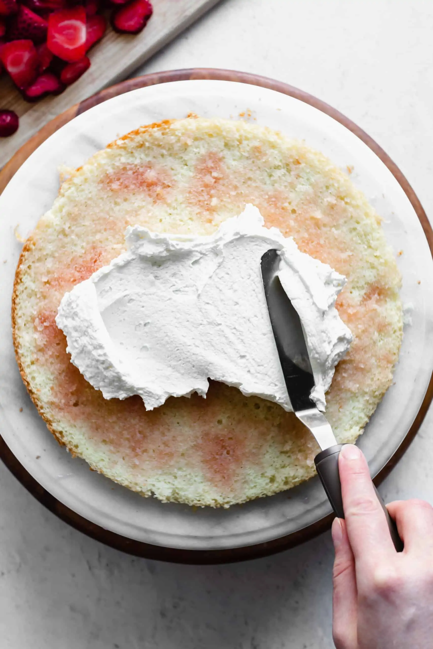 Whipped cream gets spread onto the cake layer doused with strawberry simple syrup