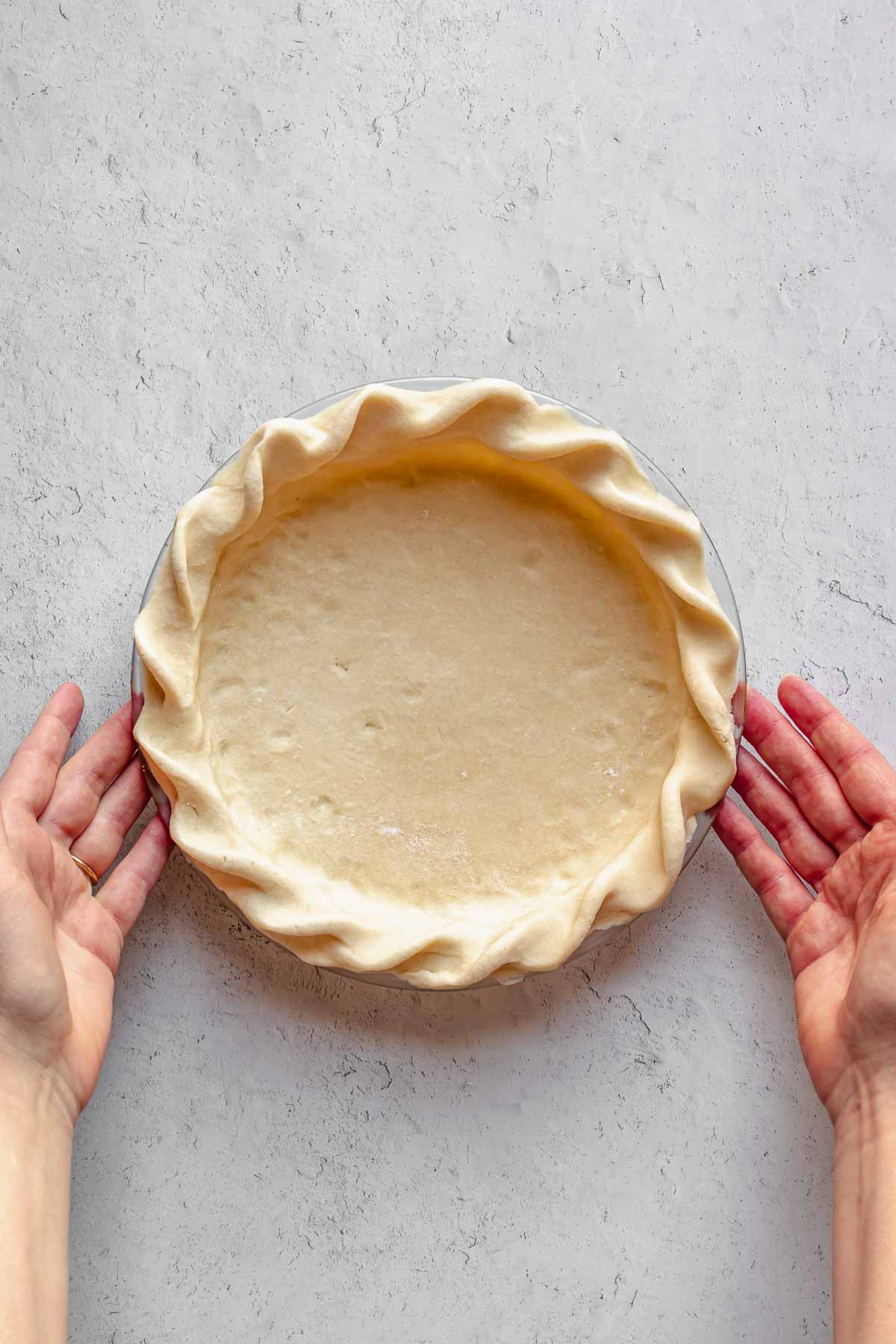 Hands hold a crimped pie crust. 