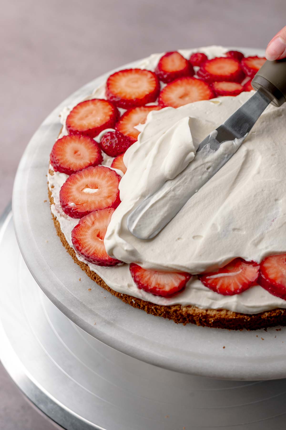 A spatula spreads whipped cream on top of strawberries.