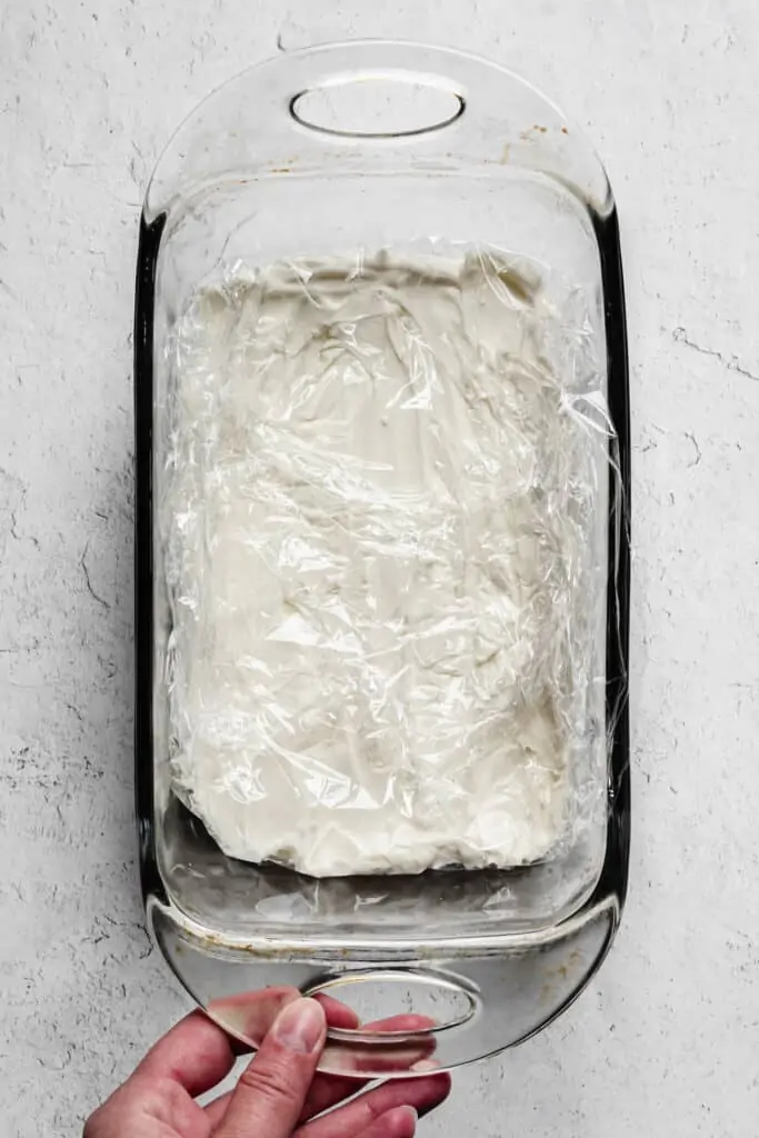 No-bake cheesecake layer in a loaf pan, wrapped in plastic wrap to freeze.