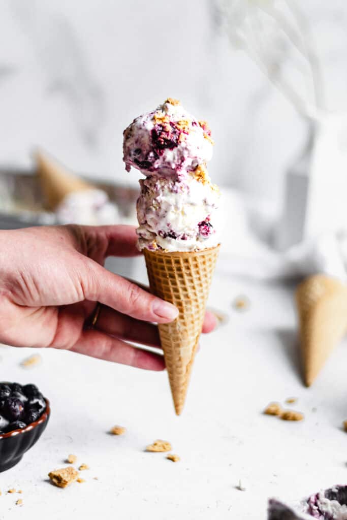 A hand holds an ice cream cone with Blueberry Cheesecake No-churn Ice Cream.