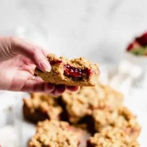 a piece of peanut butter & jelly oat bar with a bite removed to show the strawberry jam
