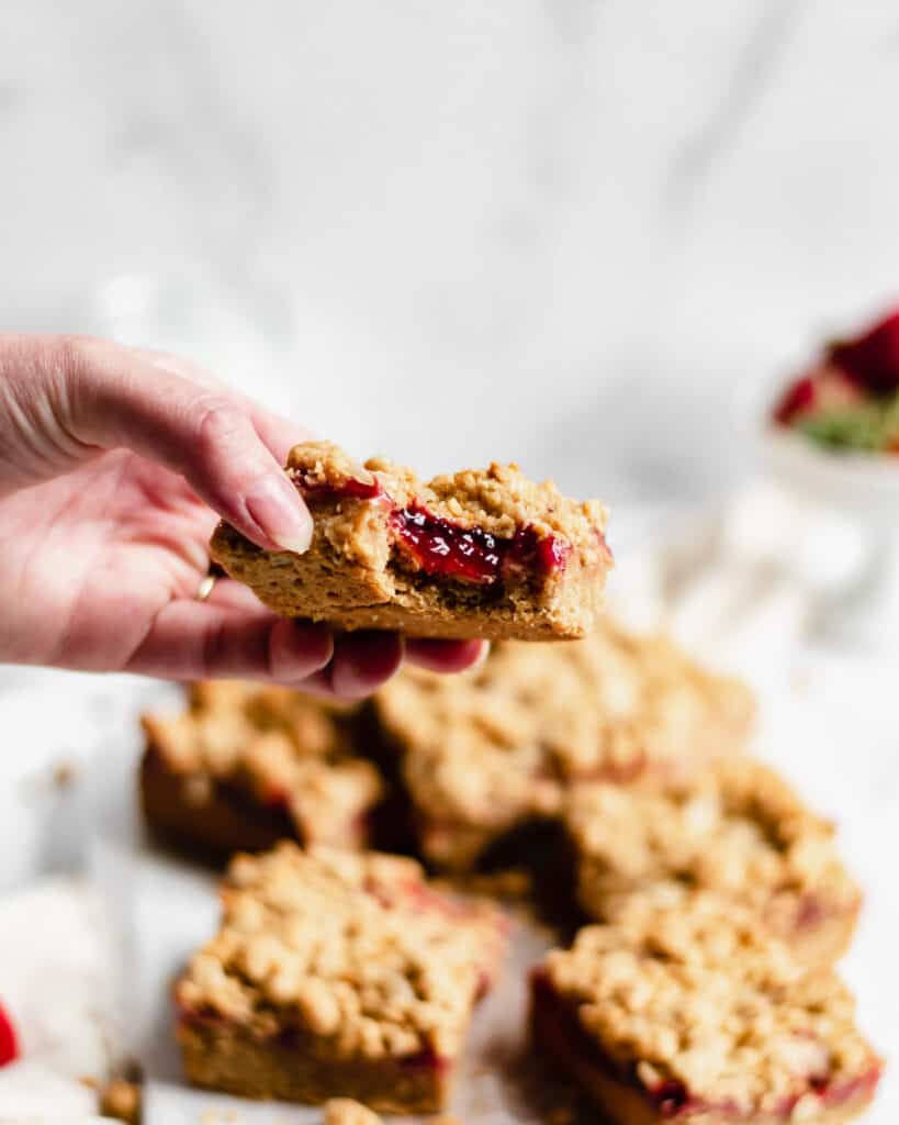 One slice of the peanut butter & jelly oat bar is held up with a bite removed to show the strawberry jam inside