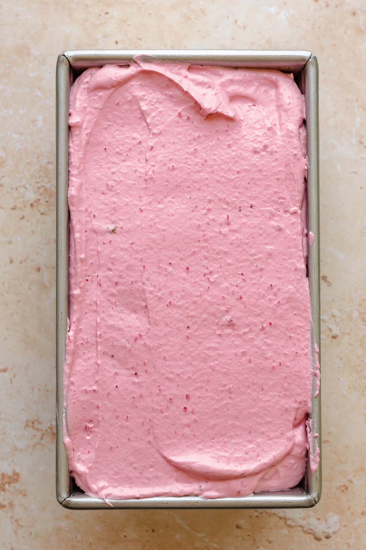 Strawberry ice cream filling a metal loaf pan.
