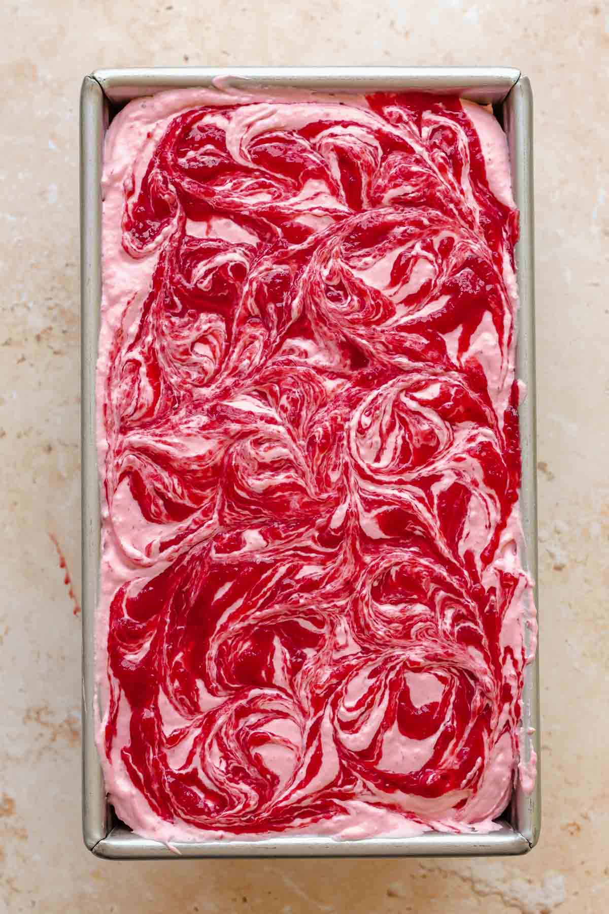 Strawberry ice cream filling a metal loaf pan. Swirls are on top.