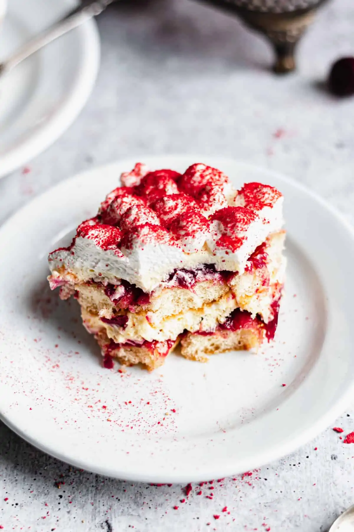 A square slice of cherry tiramisu on a plate with a bite removed.