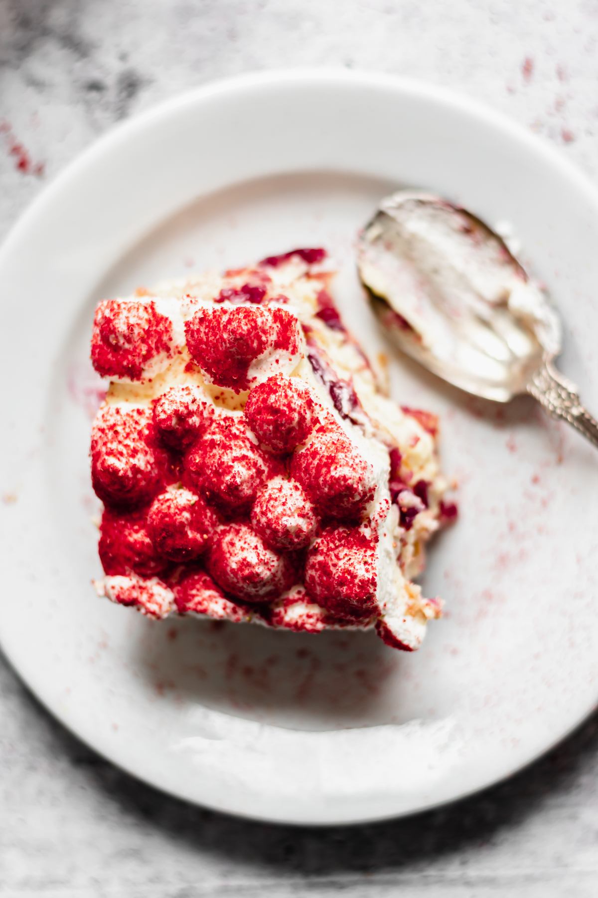A square slice of cherry tiramisu on a plate with a bite removed and the spoon on the plate.