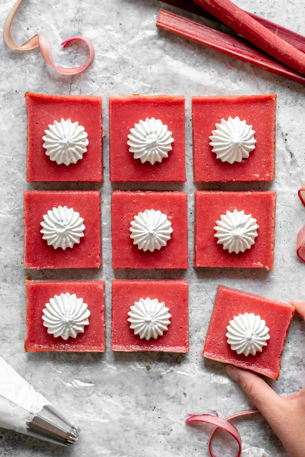 9 cut Rhubarb Curd Bars from overhead - a hand reaches in the frame to remove one