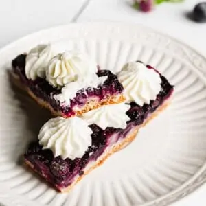 Two pieces of Blueberry Pie Bars on a plate - one has a bite removed