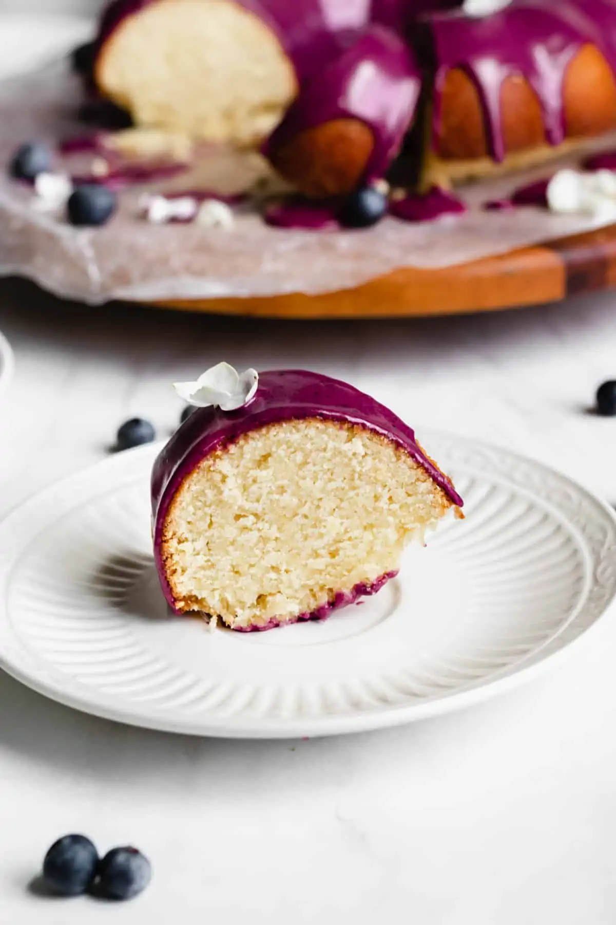 Close up straight on shot of a piece of lemon pound cake with blueberry glaze on a plate.