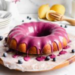 A straight on shot of lemon pound cake with blueberry glaze dripping over the edges of the cake