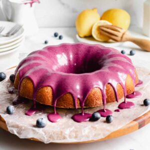 A straight on shot of lemon pound cake with blueberry glaze dripping over the edges of the cake