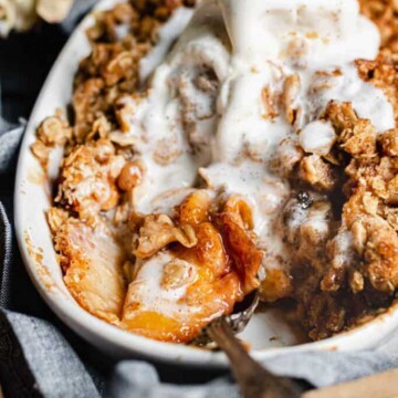 Peach crisp with melted ice cream on top and a serving spoon in the dish.