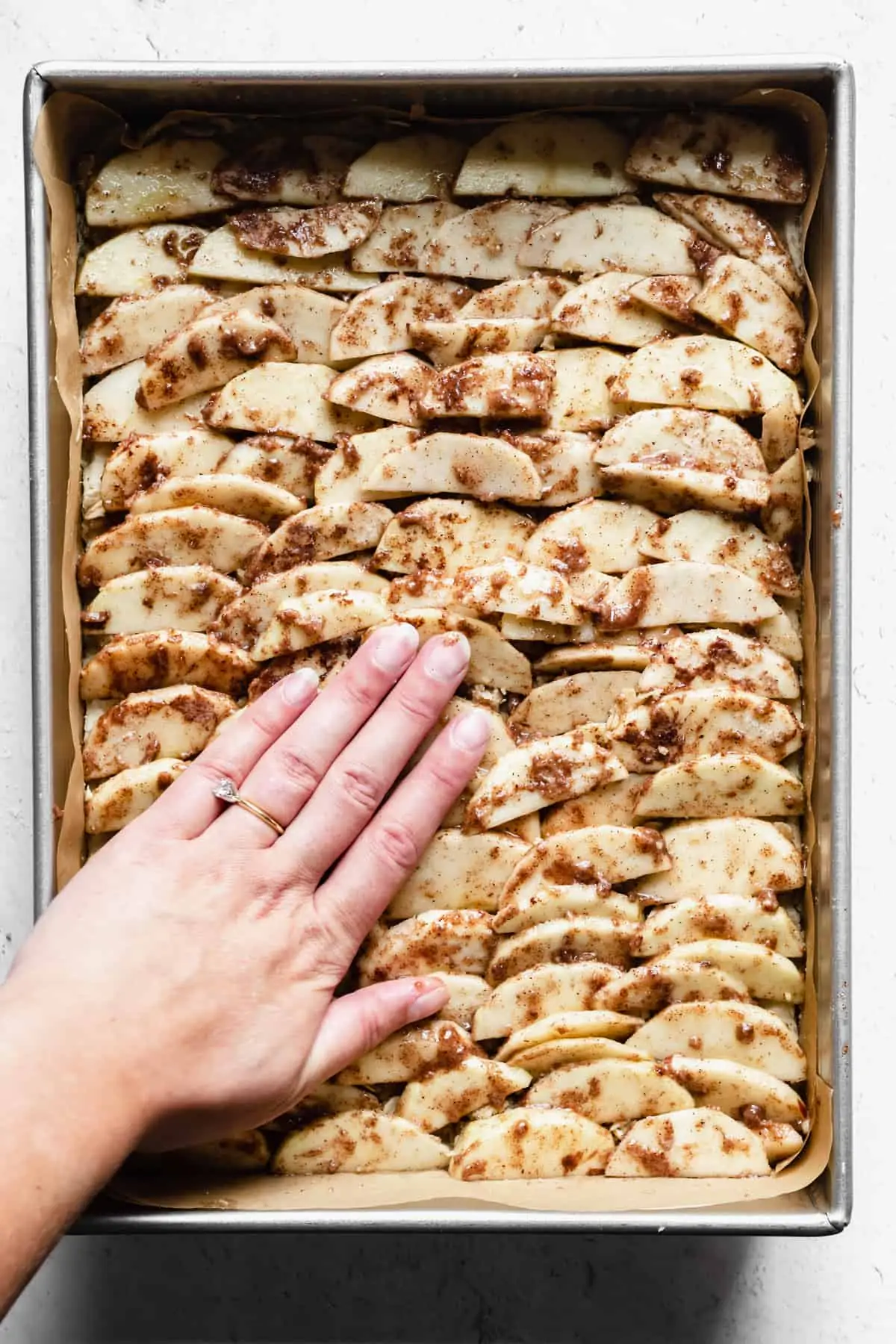 A hand presses down on apple slices layered on top of shortbread.