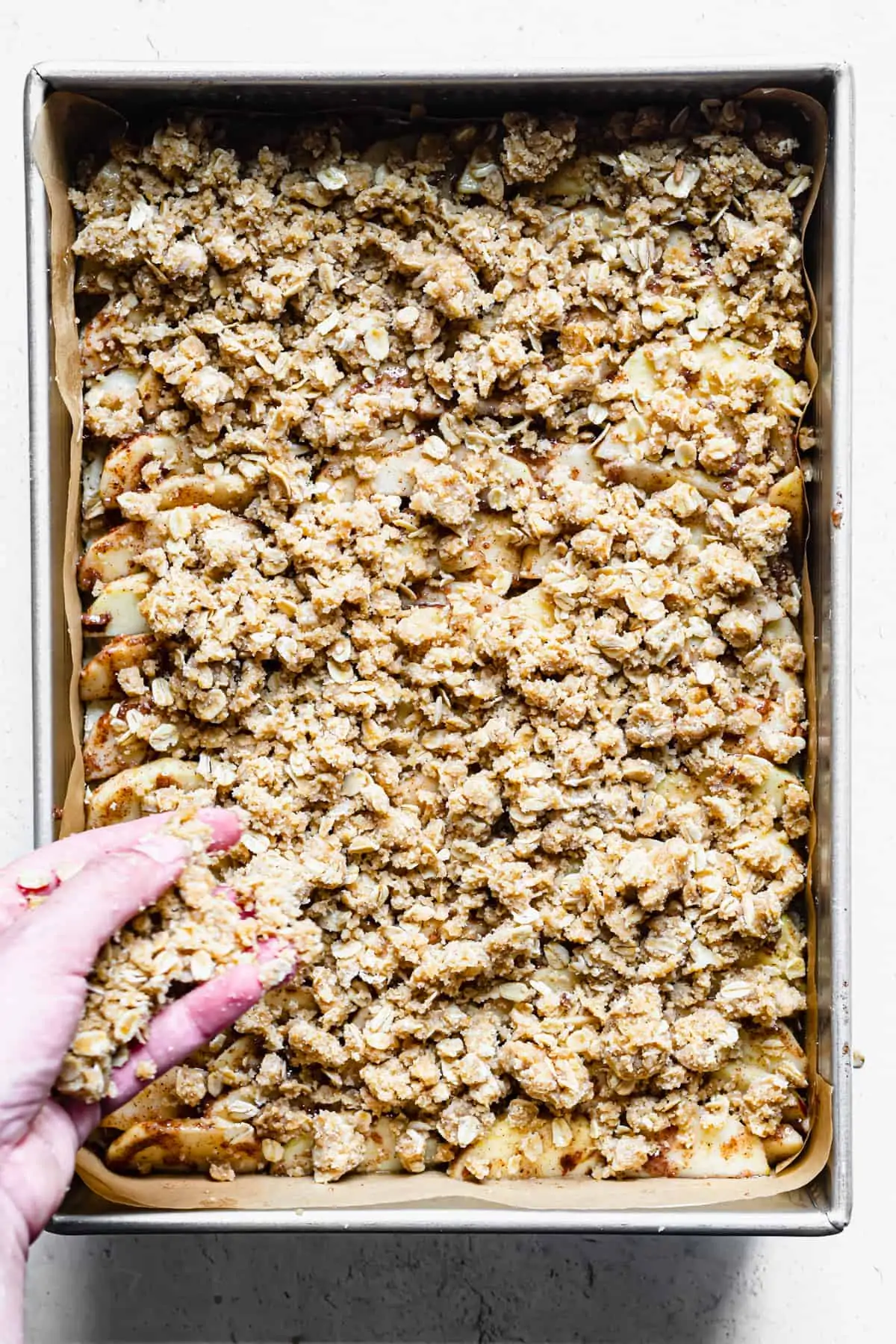 A hand sprinkles streusel topping on top of the apples.