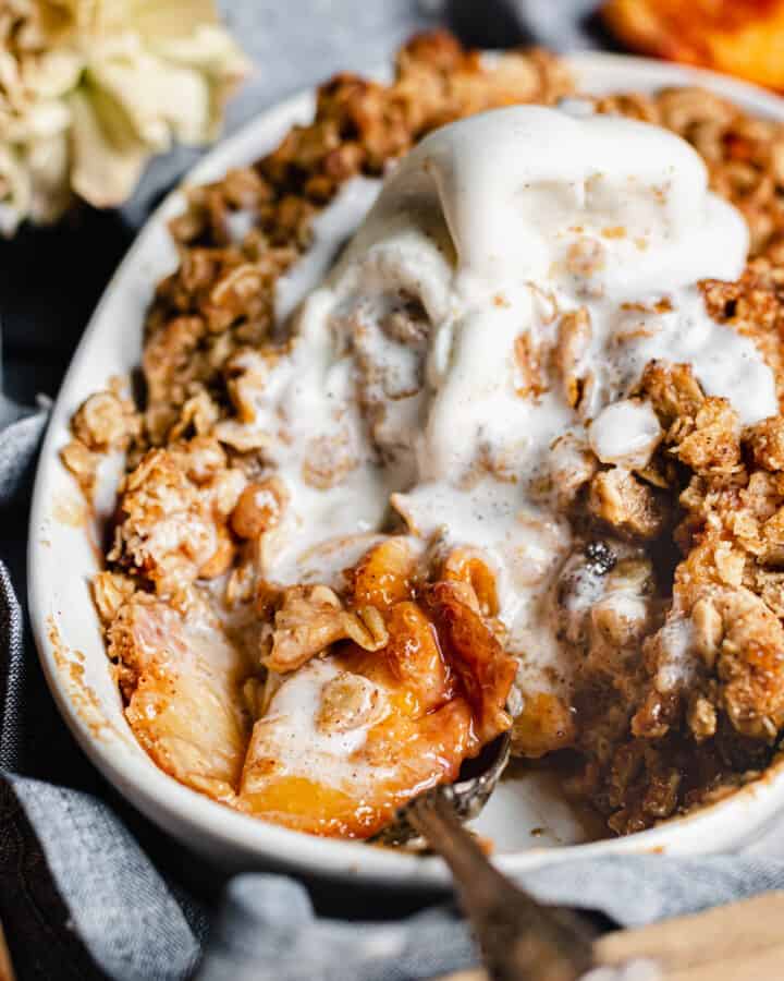 Close up shot of brown butter peach crisp with vanilla ice cream melting into it