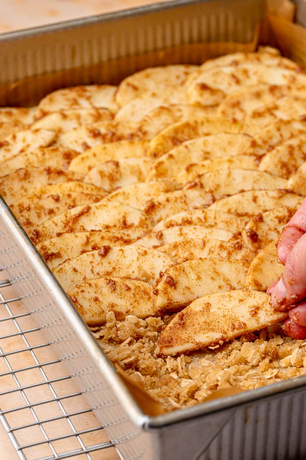 A hand lays apple slices into a pan.