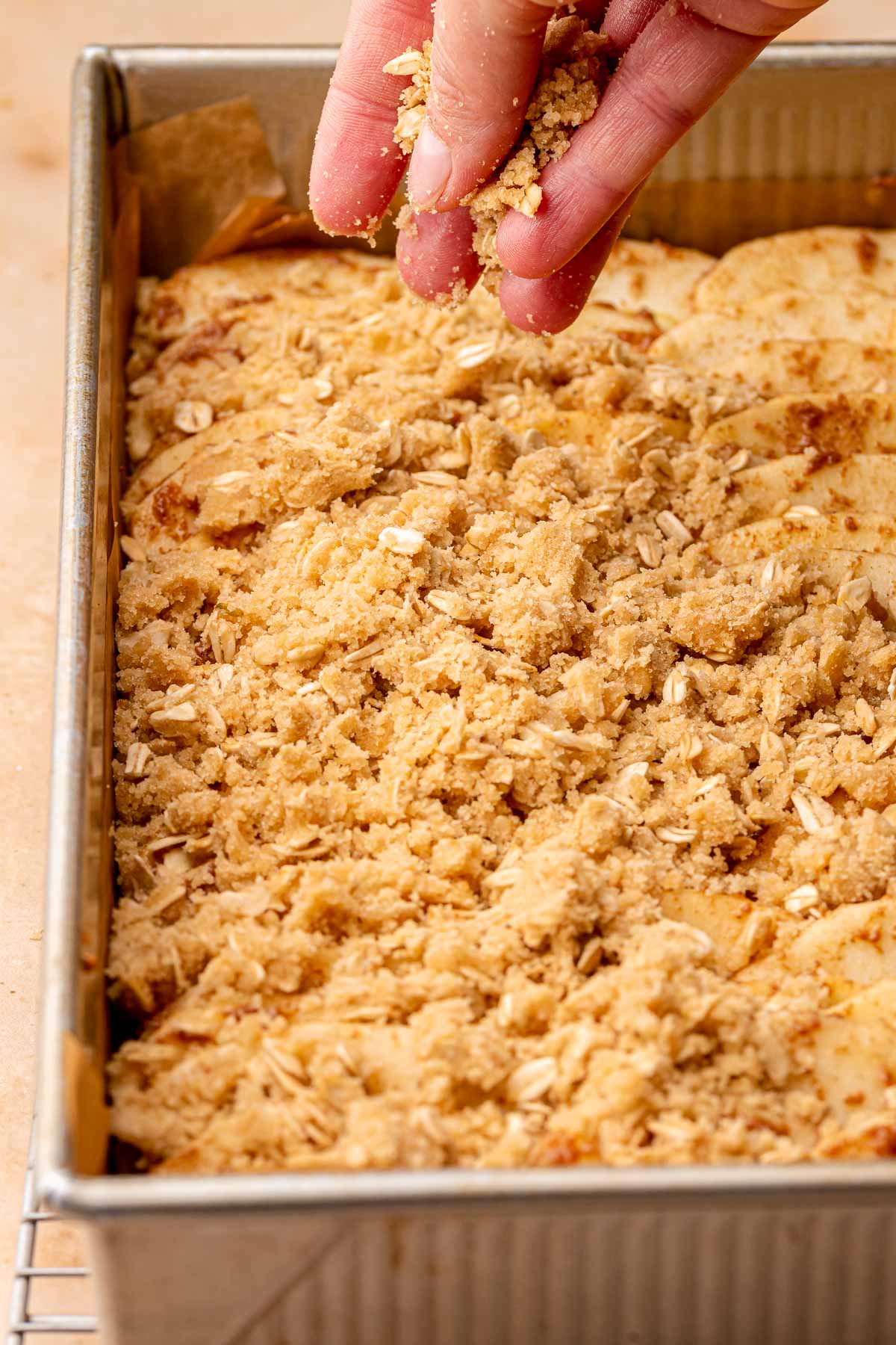 A hand sprinkles crumble topping on top of apples in a pan.