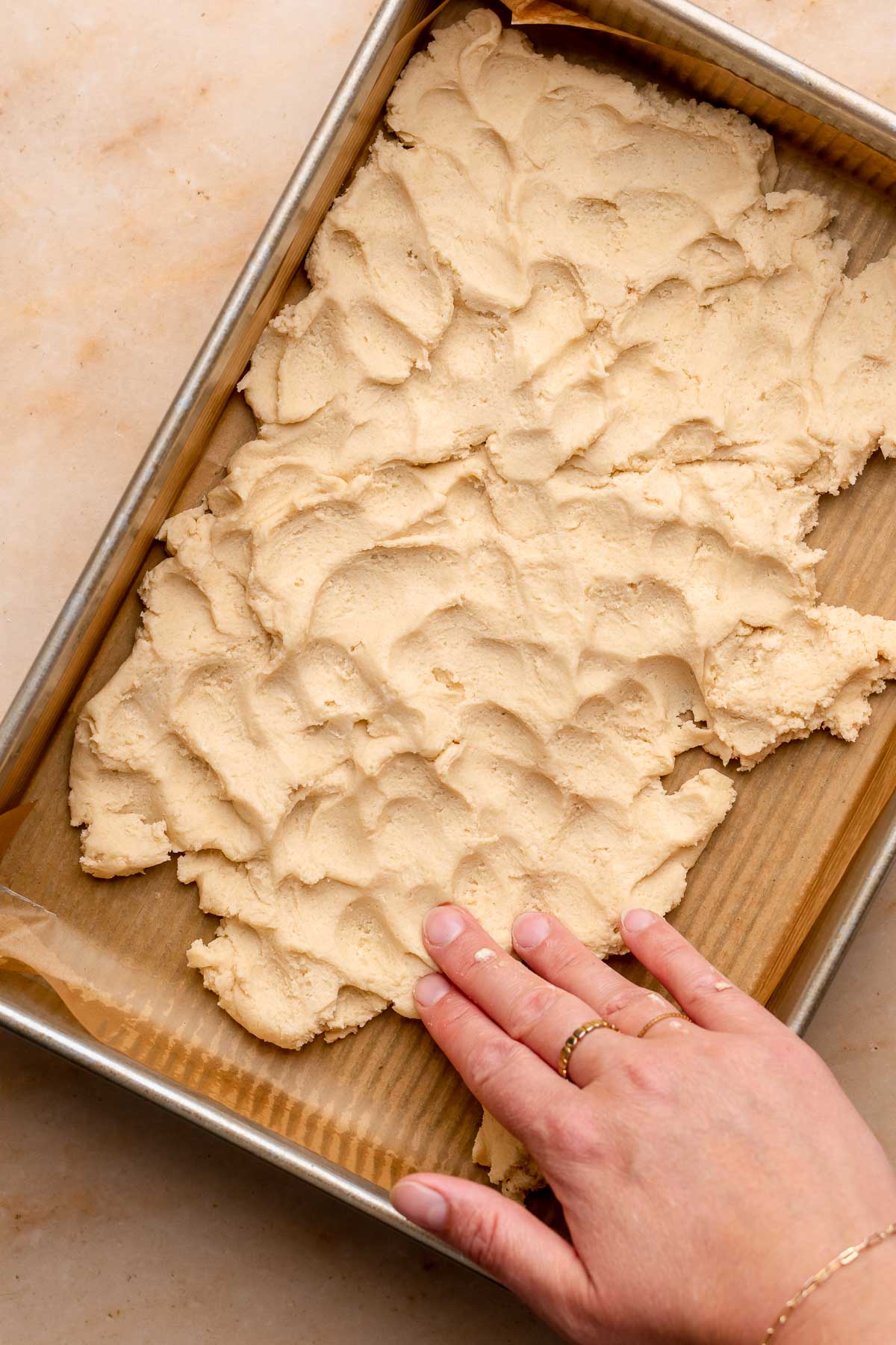 A hand presses shortbread dough into a baking pan.