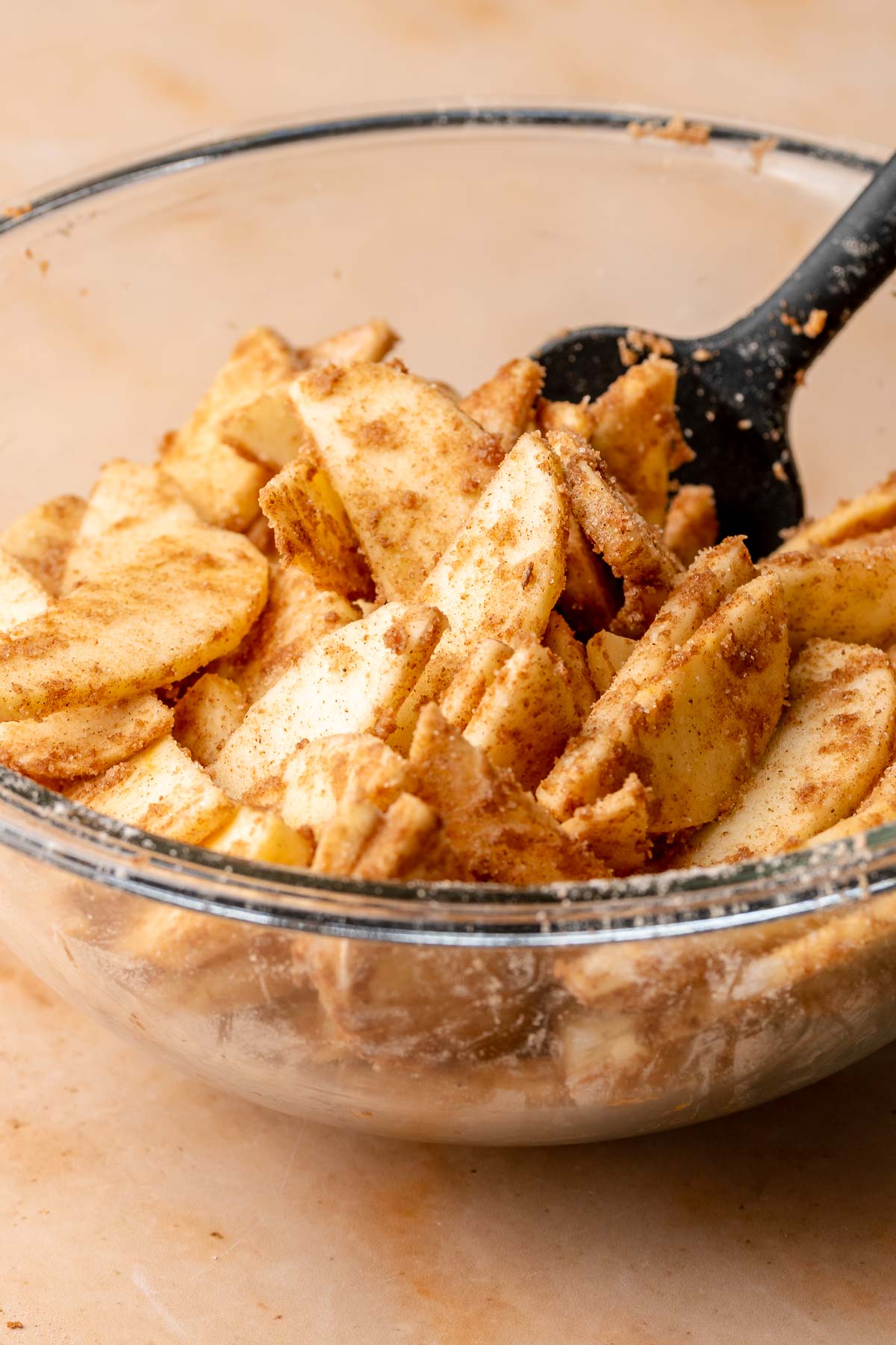 A spatula mixes spiced apples in a bowl.