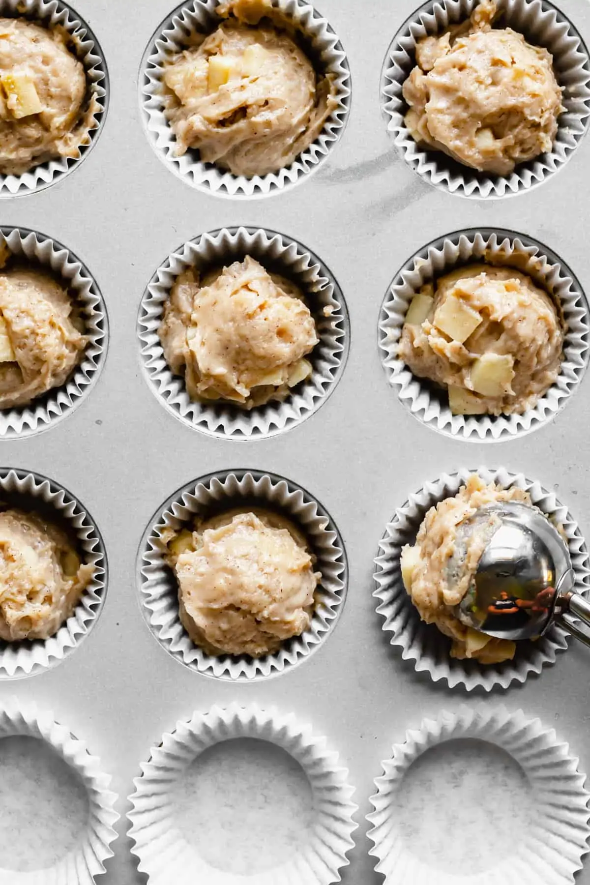 Batter being added to muffin tins with a large cookie scoop.