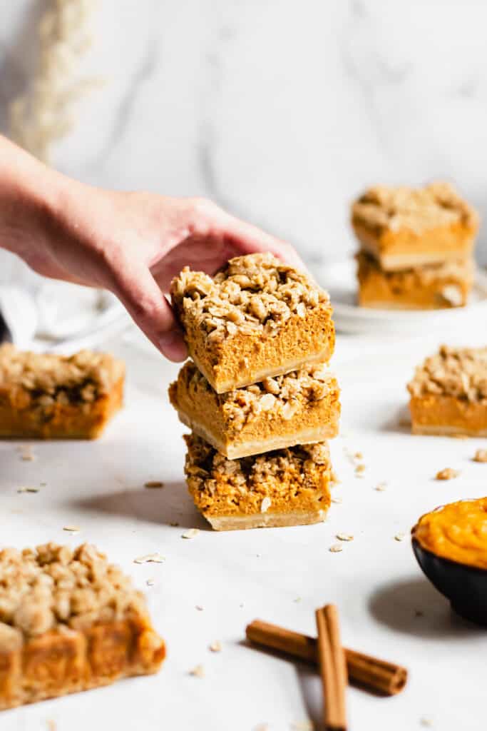 A hand reaches in the frame to remove a pumpkin pie crumble bar from a stack.