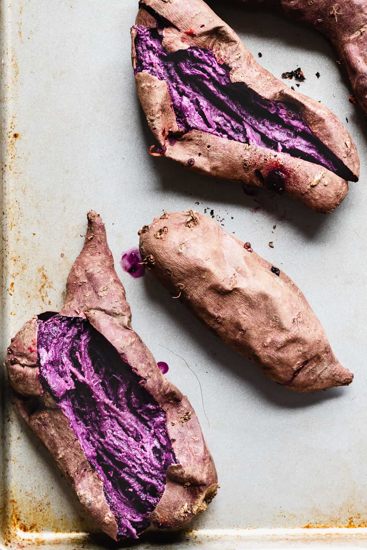 Baked purple sweet potatoes. Two are sliced open to expose the flesh.