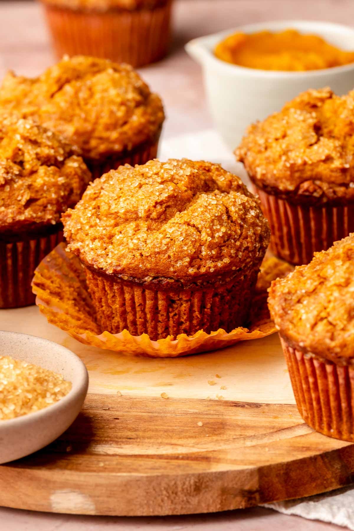 Pumpkin muffins on a platter. One has its liner pulled down.