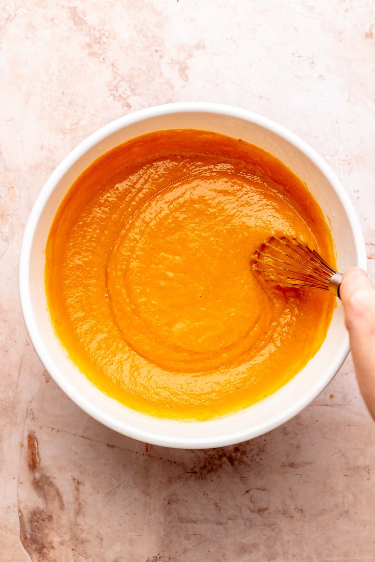 A whisk mixes pumpkin batter in a bowl.