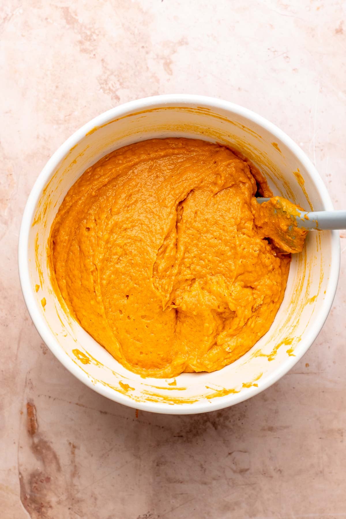 A spatula mixes pumpkin muffin batter in a bowl.