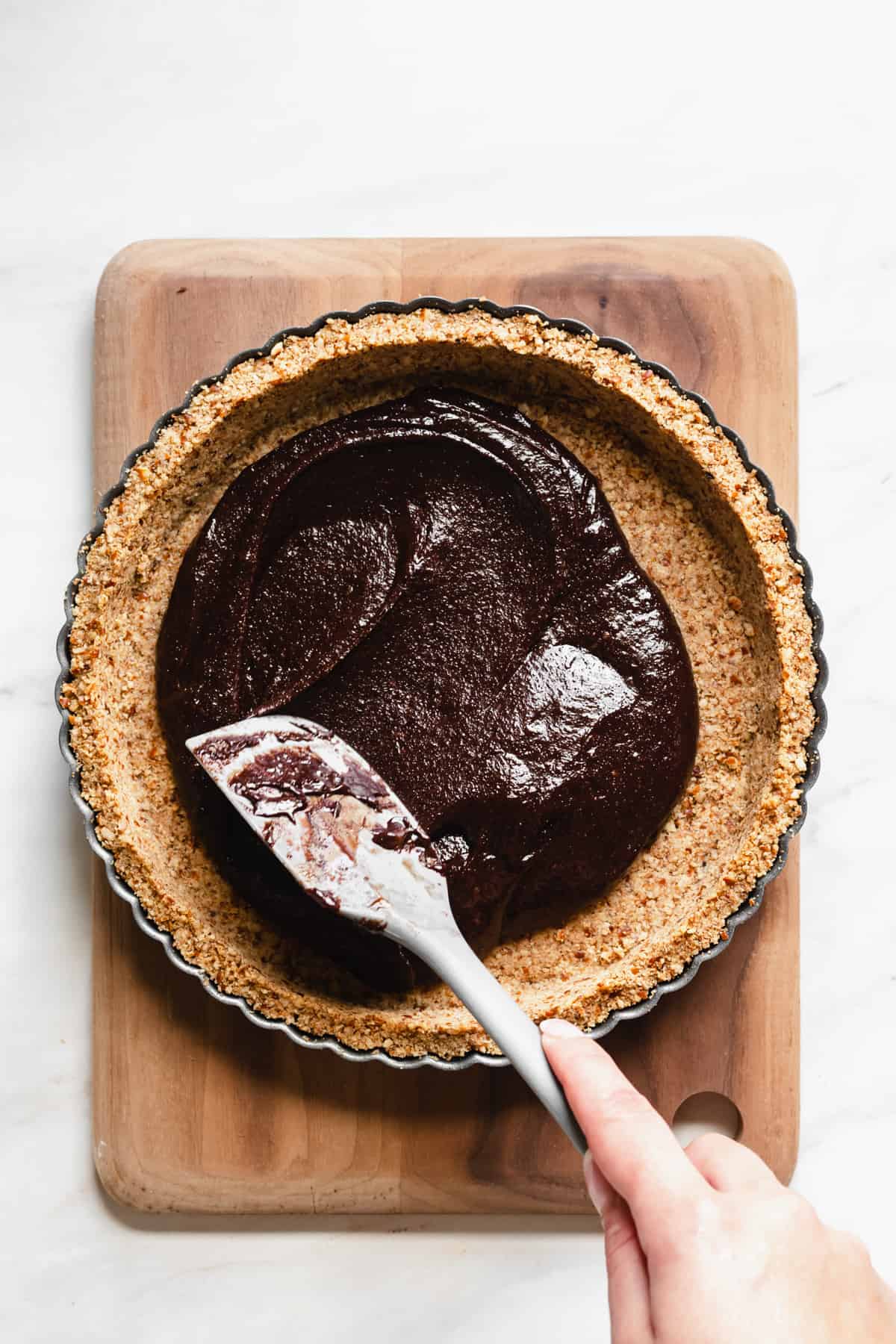 Brownie batter being spread to meet the edges of the crust