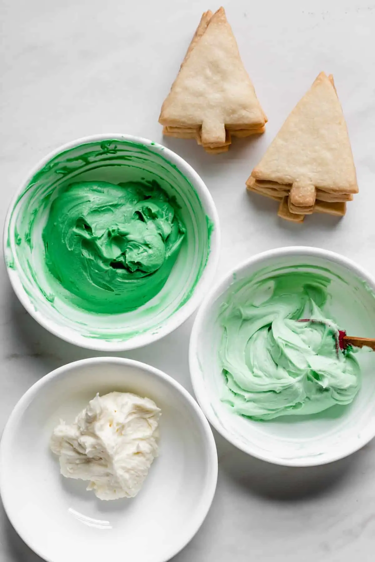 Dark green, light green, and white frosting in bowls.
