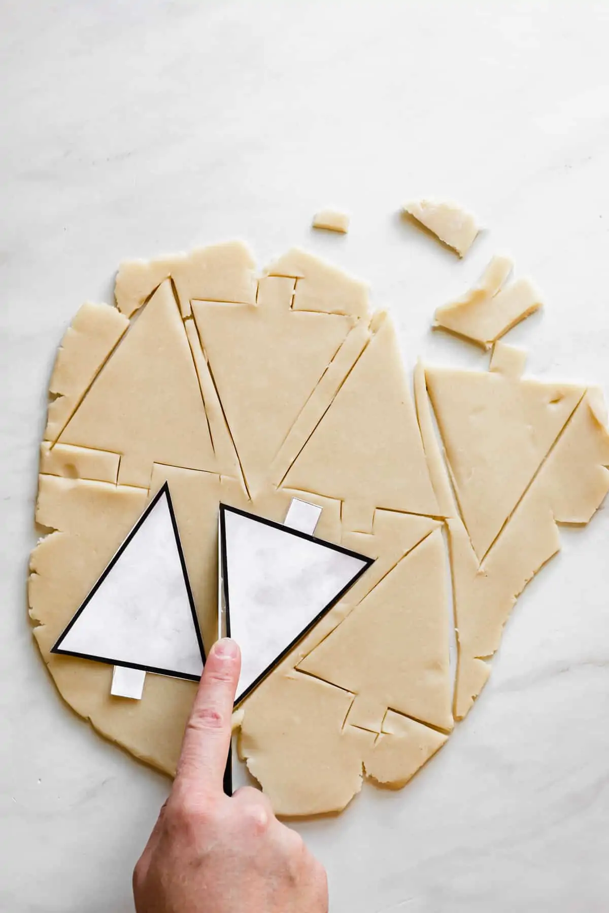 A hand cuts out Christmas tree cookies from the template