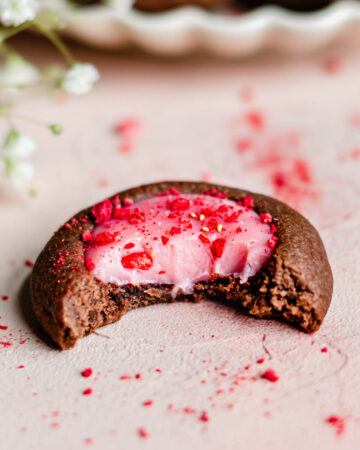A single cookie with a bite removed to show the strawberry white chocolate ganache inside.