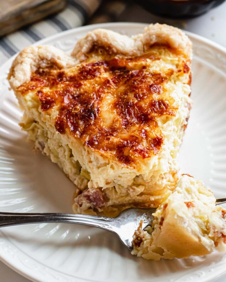 A slice of ham and Swiss quiche with the tip removed sitting on a fork