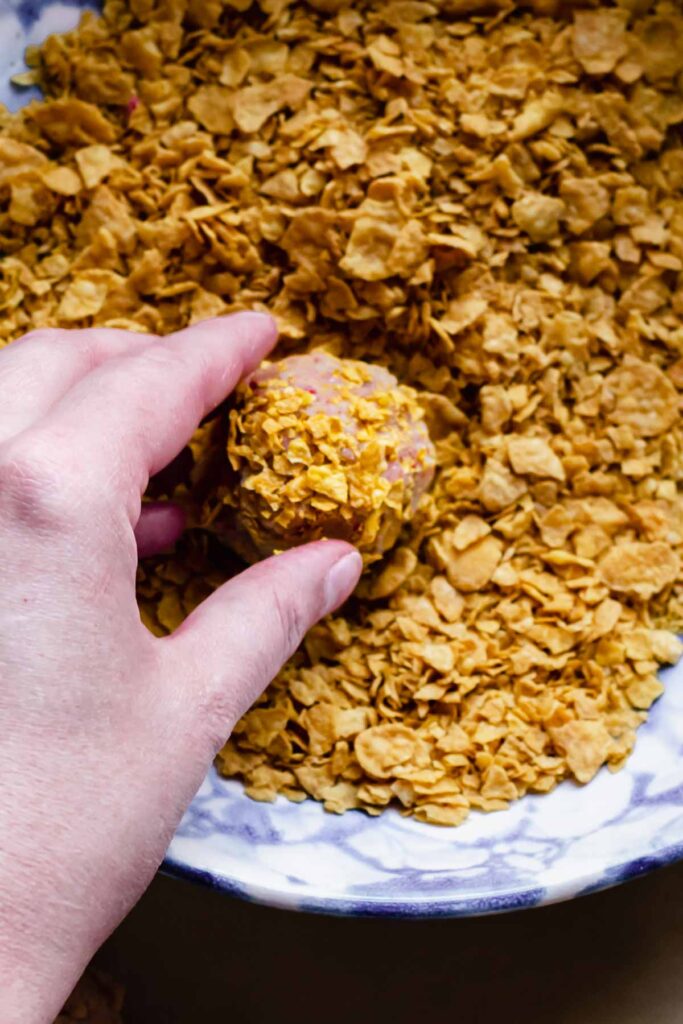 A cookie dough ball being rolled through crushed cornflakes