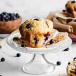 One jumbo blueberry muffin on a small pedestal cake stand.