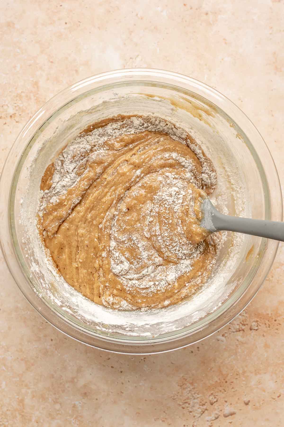 A spatula folds flour into blondie batter in a bowl.