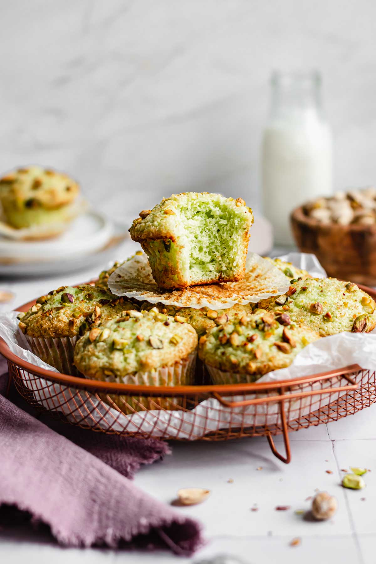 A muffin with a bite removed sits on top of a basket of pistachio muffins.