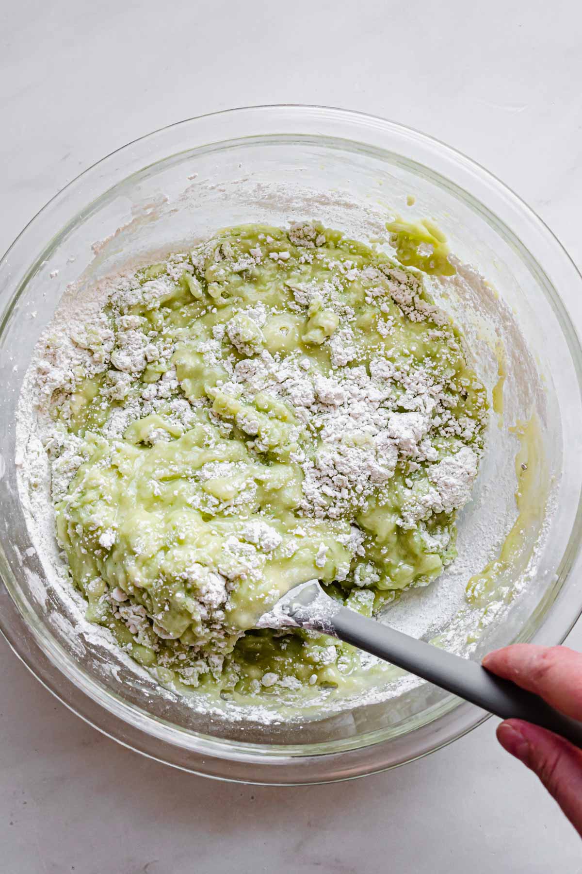 A spatula folds the batter together and starts to turn green.